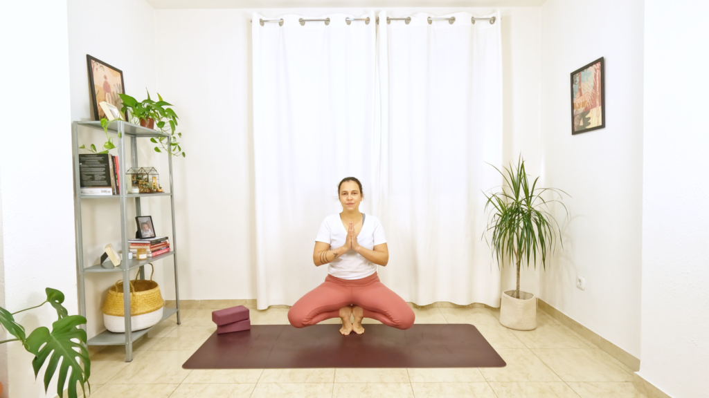 Mulher em postura de yoga com apoio nos dedos dos pés, quadril acima dos calcanhares e joelhos abertos para os lados