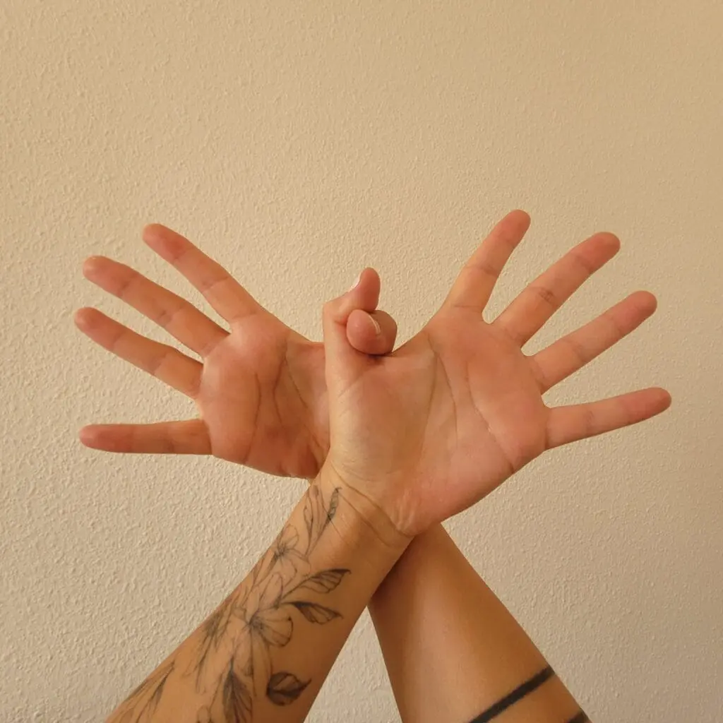 Mãos com os polegares entrelaçados e outros dedos esticados