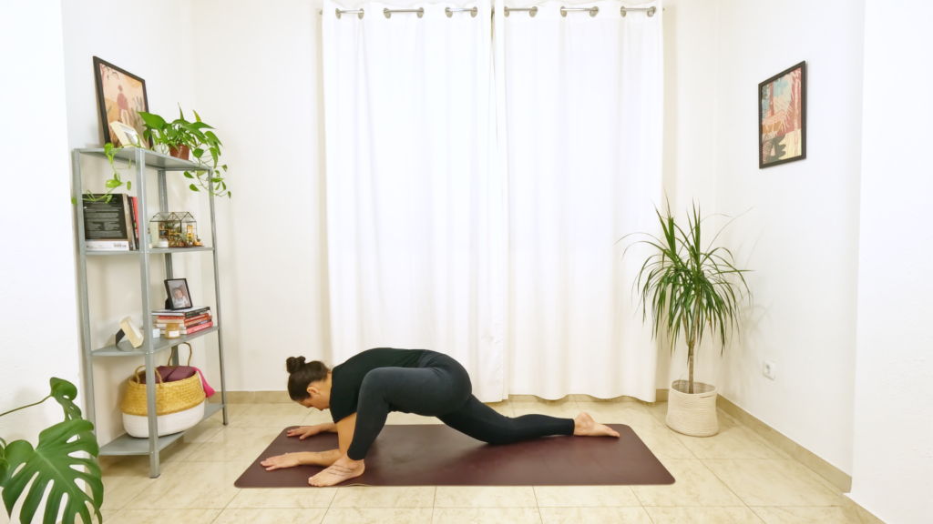Mulher em postura de yoga com um pé apoiado na frente e antebraços apoiados no chão com a outra perna esticada atrás