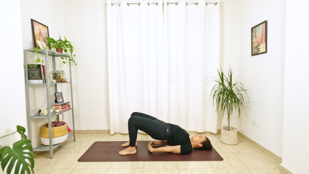 Mulher numa postura de yoga, deitada com a barriga pra cima, joelhos dobrados e pés apoiados no chão e quadril elevado