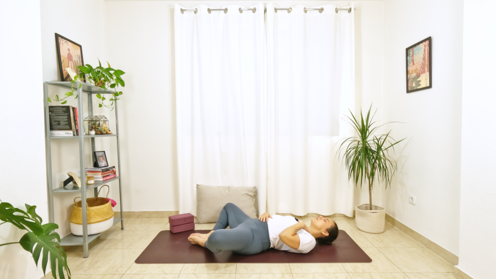 Mulher numa postura de yoga deitada com a barriga para cima com as solas dos pés unidas e os joelhos abertos para as laterais.