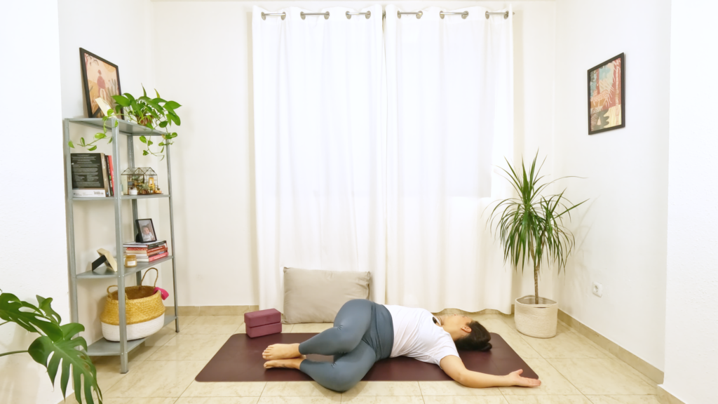 Mulher numa postura de yoga deitada com barriga para cima, com joelhos dobrados caídos para um lado e olhando para o lado oposto