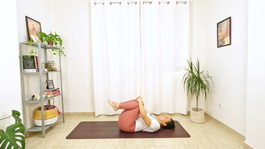 Mulher deitada no tapete de yoga abraçando os dois joelhos