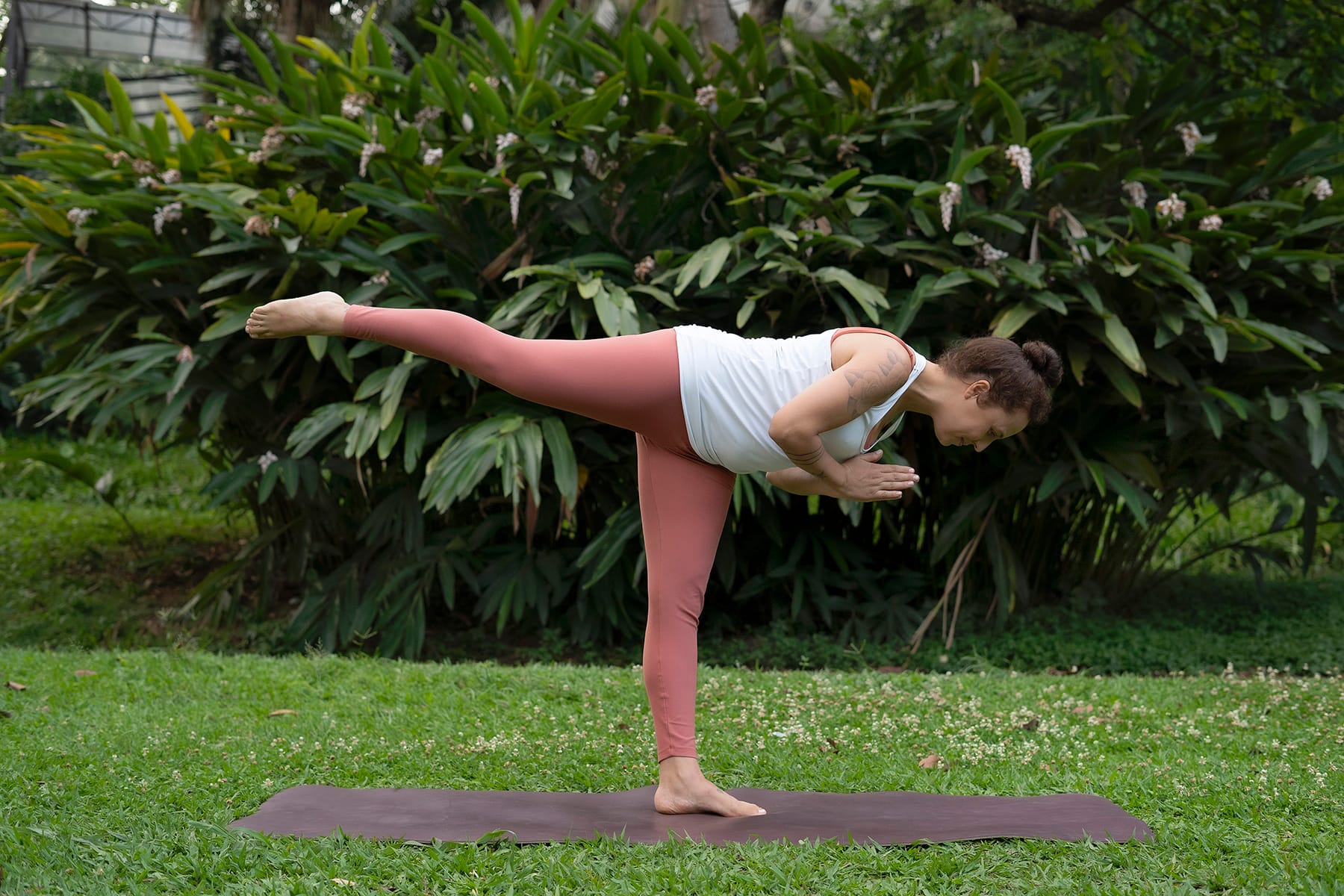 Mulher em postura de yoga equilibrando em um pé com a outra perna esticada elevada e tronco paralelo ao chão
