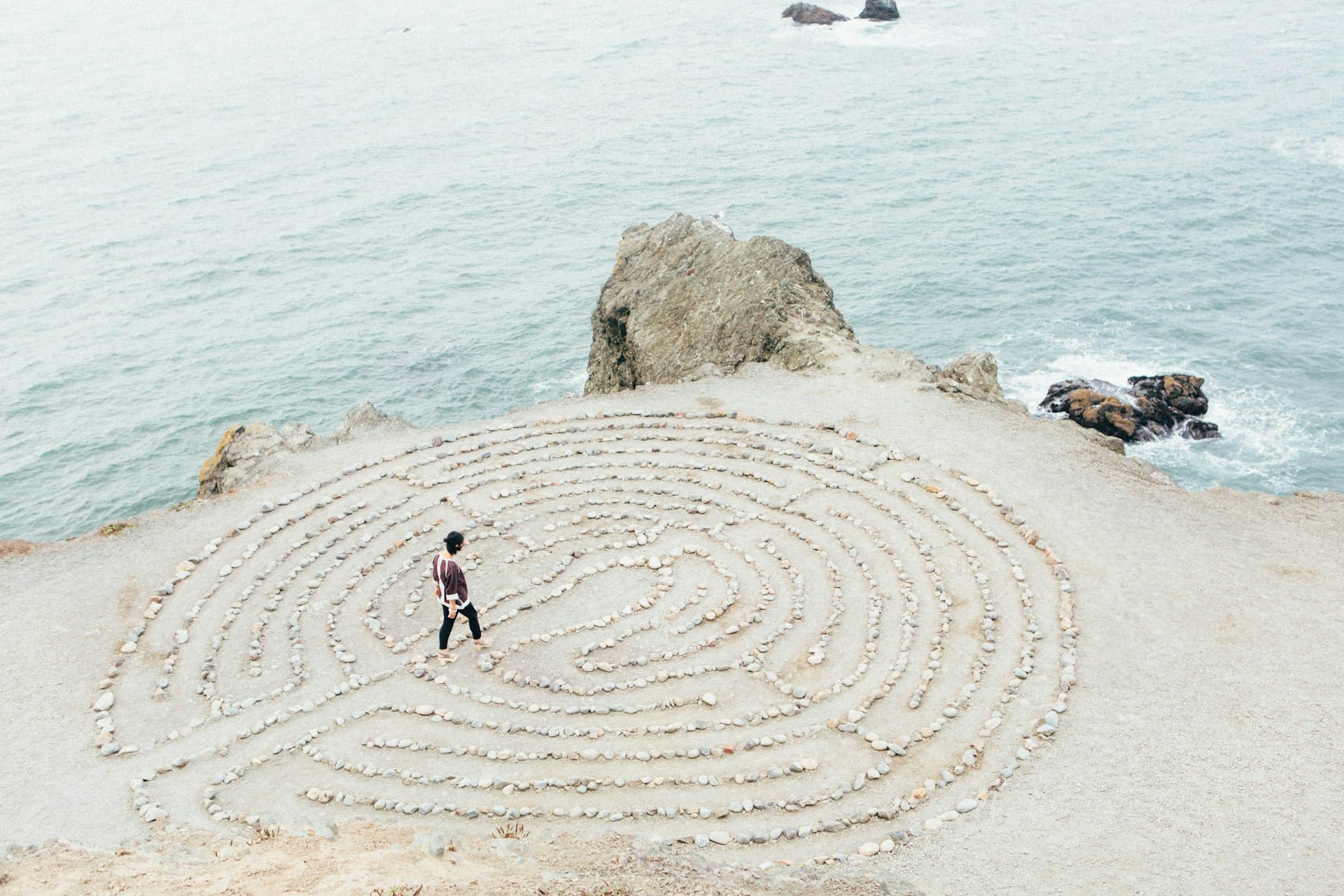 Foto de uma mulher caminhando no meio de circulos desenhados em um chão de pedras