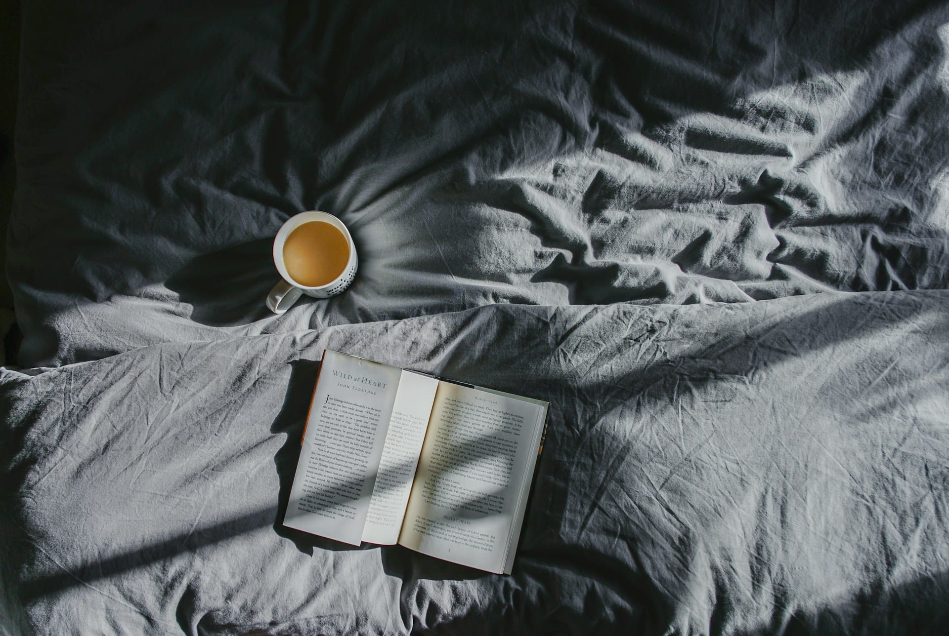 foto de um livro e uma xicara de café em cima da cama