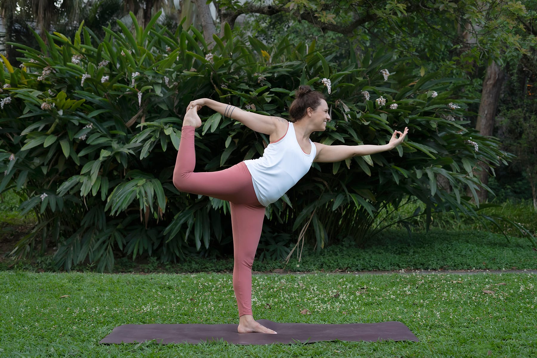 Mulher em postura de yoga com um pé apoiado e segurando o outro pé atrás com a mão
